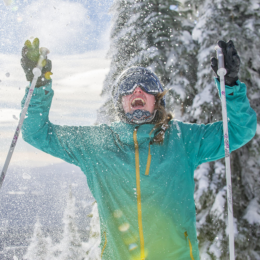 Happy skier with snowy evergreen trees in the background.
