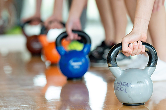 People gripping the handles of colourful kettlebells.